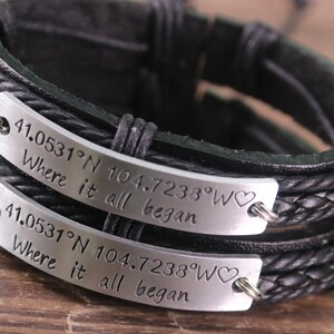 May include: Two black leather bracelets with silver metal plates engraved with the coordinates "41.0531°N 104.7238°W" and the text "Where it all began".