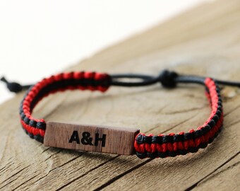 May include: A red and black braided bracelet with a wooden tag engraved with the initials "A&H".