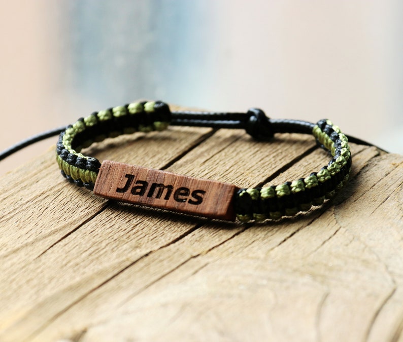 May include: A black and green braided bracelet with a wooden tag that says "James".