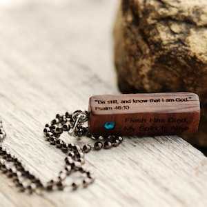 K&ouml;nnte beinhalten: Eine Holz-Halskette mit einem blauen Edelstein. Der Anh&auml;nger tr&auml;gt den Text "Sei still und wisse, dass ich Gott bin." Psalm 46:10 und "Das Fleisch ist gestorben, mein Geist lebt".