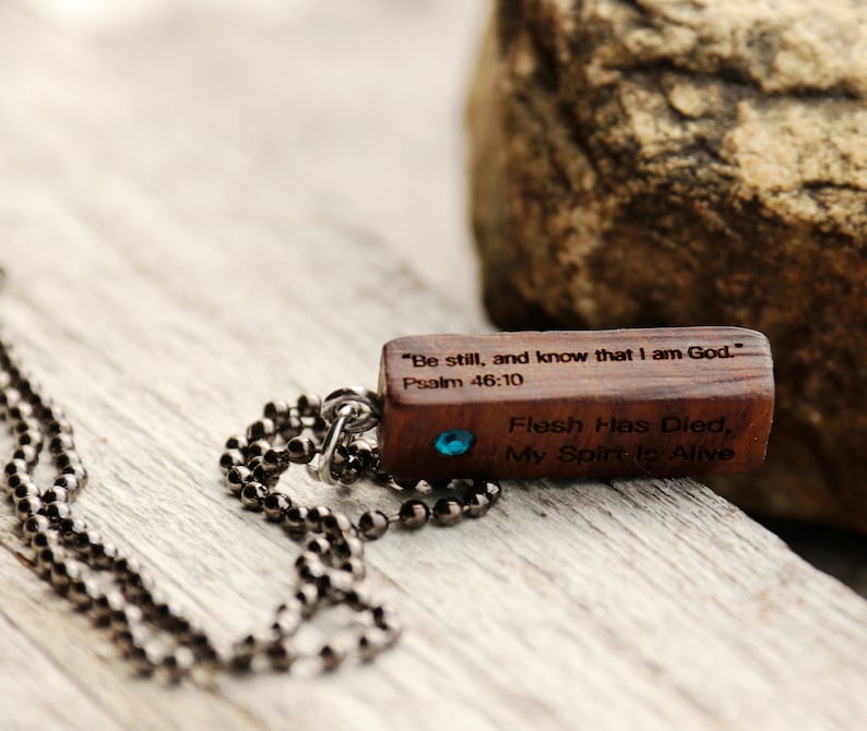 K&ouml;nnte beinhalten: Eine Holz-Halskette mit einem blauen Edelstein. Der Anh&auml;nger tr&auml;gt den Text "Sei still und wisse, dass ich Gott bin." Psalm 46:10 und "Das Fleisch ist gestorben, mein Geist lebt".