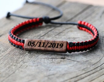 May include: A red and black braided bracelet with a wooden tag engraved with the date 05/11/2019.