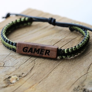 Może przedstawiać: Bransoletka pleciona w kolorze czarnym i zielonym z drewnianym znacznikiem z napisem "GAMER" czarnymi literami.