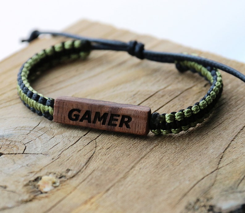 Może przedstawiać: Bransoletka pleciona w kolorze czarnym i zielonym z drewnianym znacznikiem z napisem "GAMER" czarnymi literami.