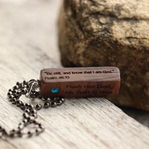 Peut inclure: Un collier avec un pendentif en bois et une pierre pr&eacute;cieuse bleue. Le pendentif porte le texte "Sois tranquille, et sache que je suis Dieu." Psaume 46:10 et "La chair est morte, mon esprit est vivant".