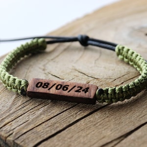 May include: A green and black braided bracelet with a wooden tag engraved with the date 08/06/24.