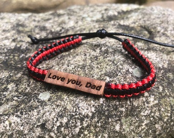 May include: A black and red braided bracelet with a wooden tag that says "Love you, Dad".
