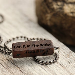 Peut inclure: Un collier en bois avec un pendentif rectangulaire qui dit "Left It In The Water" et "Jester" &agrave; l'envers. Le collier est fait d'une cha&icirc;ne argent&eacute;e.