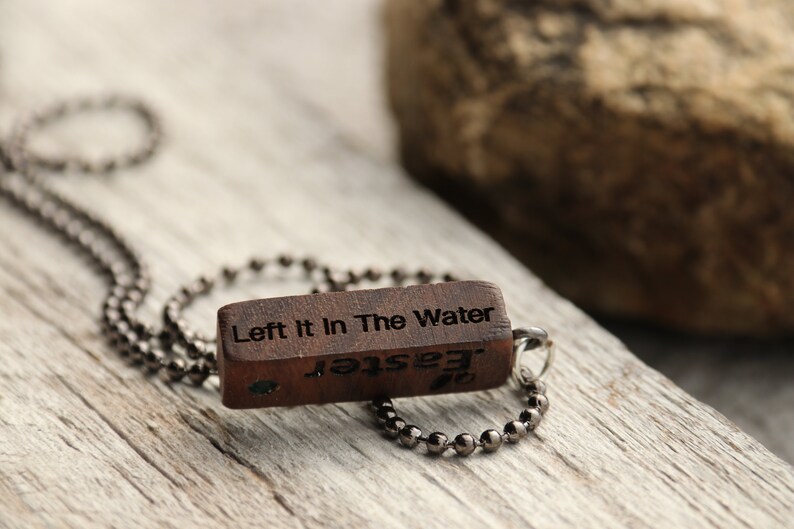Peut inclure: Un collier en bois avec un pendentif rectangulaire qui dit "Left It In The Water" et "Jester" &agrave; l'envers. Le collier est fait d'une cha&icirc;ne argent&eacute;e.