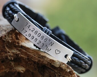 May include: Black leather bracelet with a silver plate engraved with coordinates "34.260666°N 77.998233°W" and a small heart.