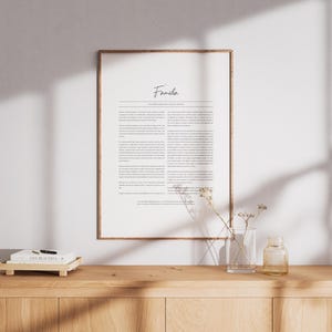Puede incluir: Una impresión enmarcada con la palabra "Famiglia" en escritura cursiva. La impresión está sobre un fondo blanco y está rodeada por un marco marrón delgado. La impresión está sentada sobre una mesa de madera con dos jarrones de vidrio transparente y un libro.