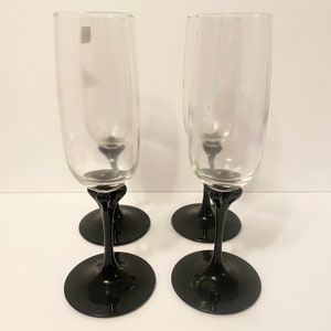 May include: Set of four champagne flutes with clear glass bowls and black stems and bases.