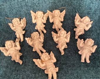 Puede incluir: Un conjunto de nueve adornos de ángel de porcelana blanca con lazos de alambre dorado para colgar. Los ángeles tienen alas, un halo y un vestido. Todos están en posición de vuelo.