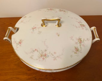 May include: White porcelain soup tureen with a lid and two handles. The tureen is decorated with a delicate floral pattern in pink and green. The handles and trim are gold.