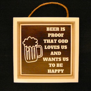 May include: A white wooden sign with a brown background and white text that reads "Beer is proof that God loves us and wants us to be happy". The sign also features a white outline of a beer mug with foam on top.