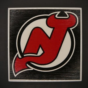 May include: A black and white square sign with a red and white New Jersey Devils logo. The logo is a stylized letter N with a devil's tail.