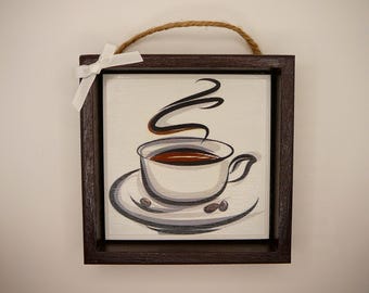 May include: A brown wooden frame with a white background and a drawing of a coffee cup with steam rising from it. The cup is on a saucer with coffee beans around it.
