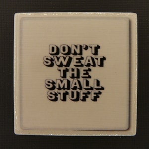 May include: A white square sign with a black border and the text "DON'T SWEAT THE SMALL STUFF" in a 3D-style font.