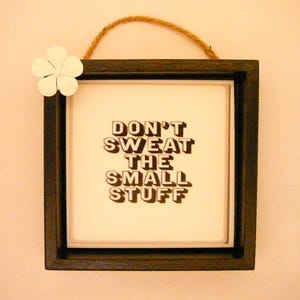 May include: A black framed picture with a white background and the text "Don't sweat the small stuff" in brown letters.