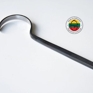 Puede incluir: Una herramienta de gancho de metal negro con un mango curvo y un borde afilado. La herramienta está hecha en Lituania, como lo indica la etiqueta en la herramienta.