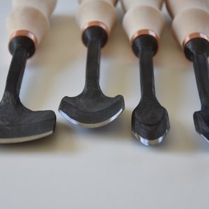 May include: Set of four wood carving tools with black metal blades and wooden handles with copper accents.