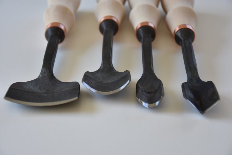 May include: Set of four wood carving tools with black metal blades and wooden handles with copper accents.