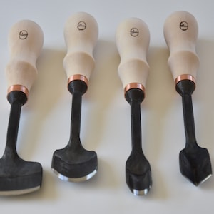 May include: Set of four wood handled carving tools with black metal blades. The blades have different shapes, including a curved, a pointed, and a square shape.