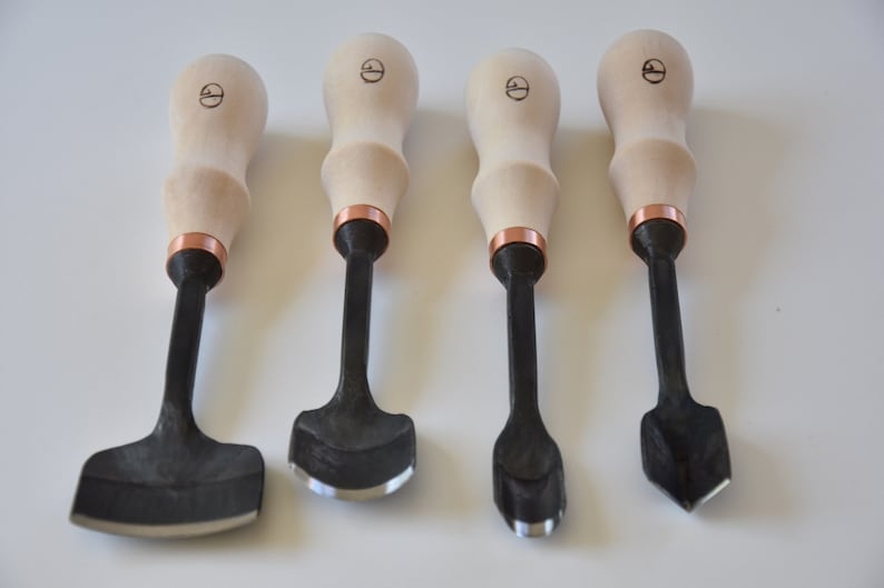 May include: Set of four wood handled carving tools with black metal blades. The blades have different shapes, including a curved, a pointed, and a square shape.