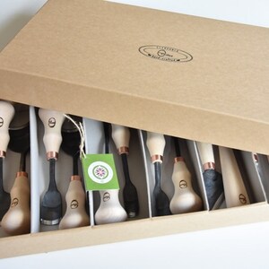 May include: A set of 10 wood carving tools with wooden handles and copper accents, neatly arranged in a brown cardboard box.