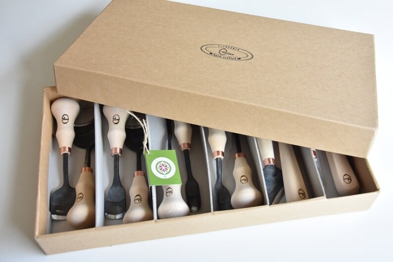May include: A set of 10 wood carving tools with wooden handles and copper accents, neatly arranged in a brown cardboard box.
