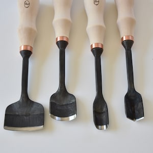 May include: Set of four wood carving tools with wooden handles and copper accents. The tools have different shaped blades for carving wood.