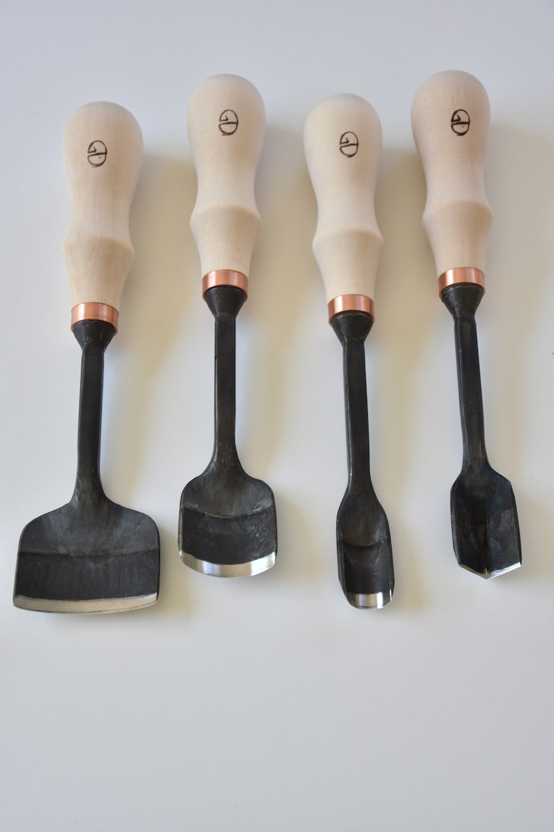 May include: Set of four wood carving tools with wooden handles and copper accents. The tools have different shaped blades for carving wood.