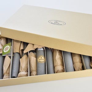 May include: A cardboard box with a lid open, revealing a set of 10 gray cylindrical objects wrapped in brown paper. The objects are arranged in rows within the box. The box is labeled "Handmade" and "Liberty Craft Supplies".