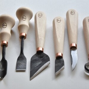 May include: Set of seven wood carving tools with wooden handles and copper accents. The tools have different blade shapes for various carving techniques.