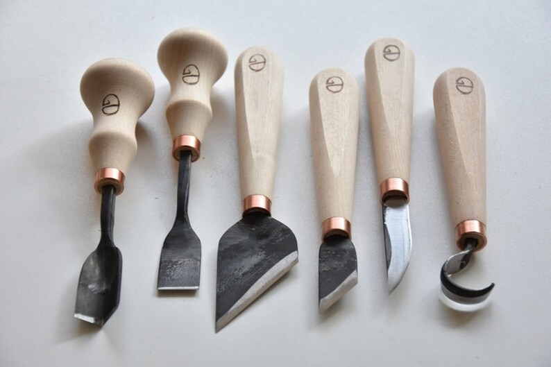 May include: Set of seven wood carving tools with wooden handles and copper accents. The tools have different blade shapes for various carving techniques.