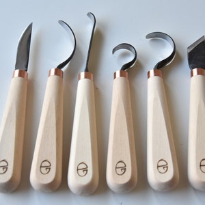May include: Set of seven wood carving tools with copper accents and wooden handles. The tools have different blade shapes for various carving techniques.