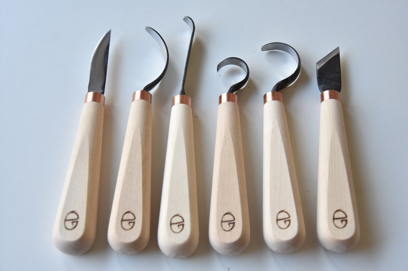 May include: Set of seven wood carving tools with copper accents and wooden handles. The tools have different blade shapes for various carving techniques.