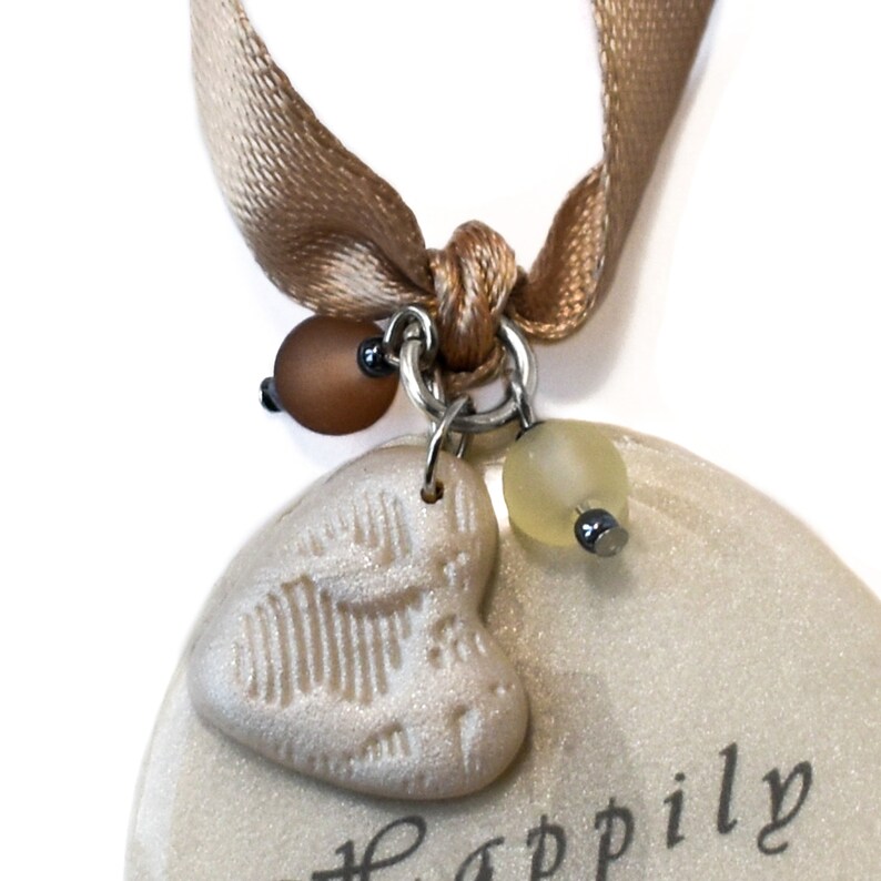 Closeup of embossed heart charm and brown and off white Czech beads hanging from satin ribbon.