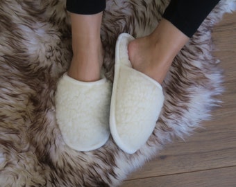 May include: Pair of white sheepskin slippers with a fluffy texture. The slippers are worn on a brown and white faux fur rug.