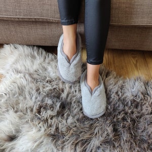 May include: A pair of grey fluffy slippers with a V-shaped opening at the top. The slippers are on a fluffy grey rug.