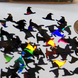 May include: A scattering of black witch hat shaped iridescent glitter, approximately the size of a US dime.