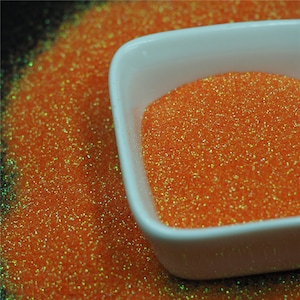 May include: A small white bowl filled with orange glitter. The glitter has a slight iridescent sheen.