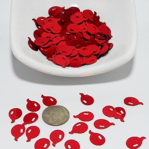 May include: Red balloon-shaped confetti scattered on a white surface and in a white dish. A U.S. dime is next to the confetti for size comparison. The confetti has a shiny, metallic finish and a small rectangular cutout.