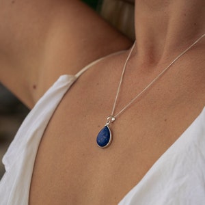 May include: A silver chain necklace with a teardrop-shaped pendant featuring a dark blue lapis lazuli stone.