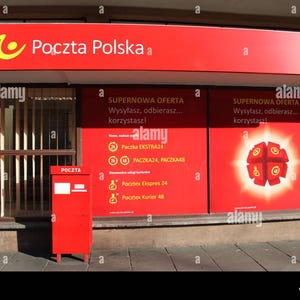May include: A bright red Poczta Polska post office storefront featuring a prominent red sign with a yellow logo. A matching red metal mailbox stands in front of the window, which displays red signage with white text and a graphic of a red cube.