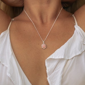 May include: A silver chain necklace with a pink gemstone pendant. The pendant is a hexagonal shape with a smooth, rounded surface.