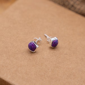 May include: A pair of silver stud earrings with hexagonal purple gemstone accents.