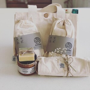 May include: A set of reusable produce bags, a tote bag, and a bar of soap in a glass jar. The bags are made of natural fabric and have the text "sumki produce bags" printed on them. The tote bag has a brown button closure.