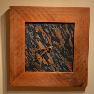 Peut inclure: Une horloge carrée avec un cadran en métal cuivre et noir. L'horloge est encadrée d'un cadre en bois foncé.