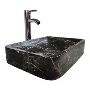 Puede incluir: Un lavabo de baño de mármol marrón oscuro con un grifo cromado. El lavabo tiene forma cuadrada y una superficie lisa y pulida.